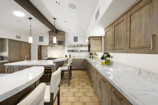 kitchen with light stone countertops, a kitchen breakfast bar, decorative light fixtures, a center island with sink, and vaulted ceiling with beams