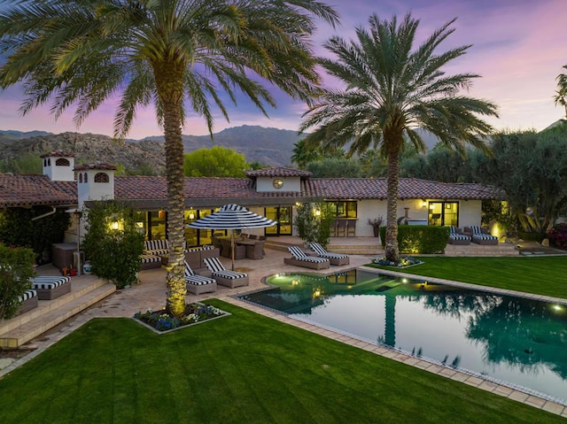 pool at dusk with a lawn, a patio area, and a mountain view