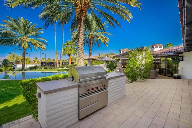 view of patio with a swimming pool, a water view, grilling area, and exterior kitchen