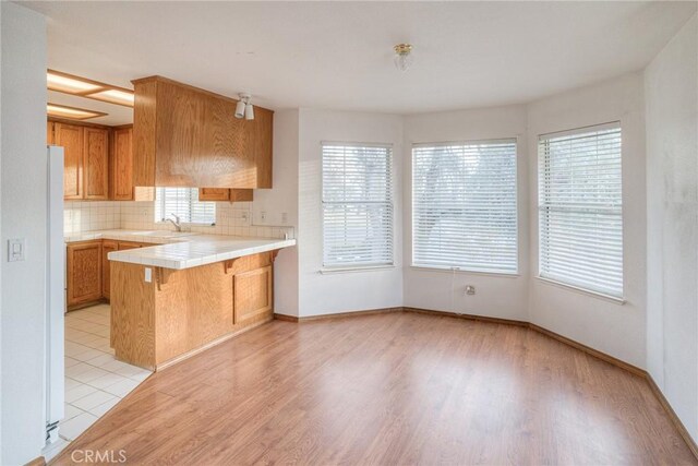 kitchen featuring tile countertops, light wood-type flooring, kitchen peninsula, and tasteful backsplash