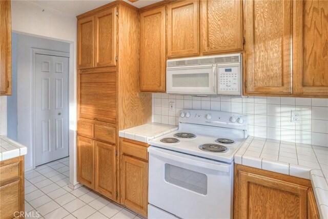 kitchen with tile countertops, white appliances, backsplash, and light tile patterned floors