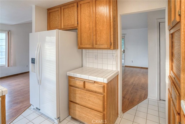 kitchen featuring tile counters, light hardwood / wood-style floors, decorative backsplash, and white refrigerator with ice dispenser