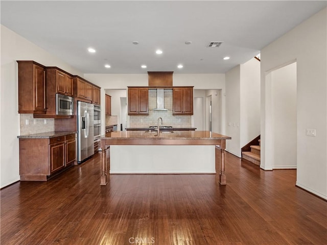 kitchen featuring an island with sink, stainless steel appliances, dark hardwood / wood-style floors, and wall chimney range hood