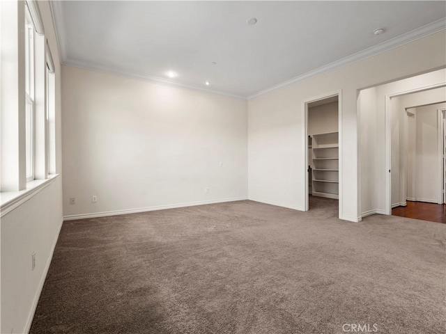 unfurnished bedroom with a spacious closet, ornamental molding, and dark colored carpet