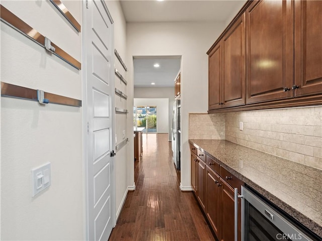 interior space with tasteful backsplash, stainless steel refrigerator, dark hardwood / wood-style floors, dark stone counters, and beverage cooler