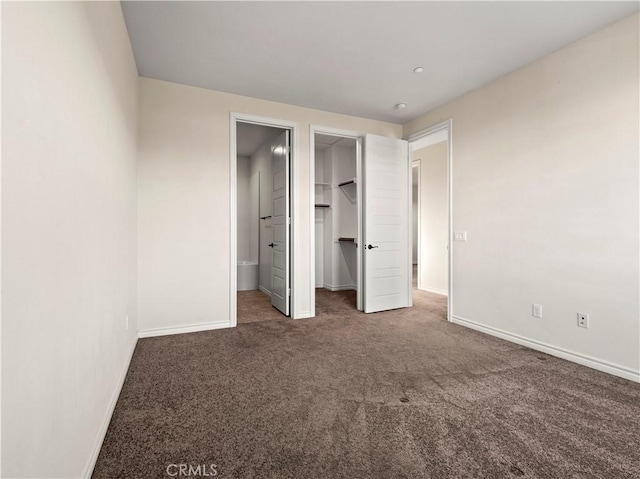 unfurnished bedroom with dark colored carpet, a walk in closet, and a closet