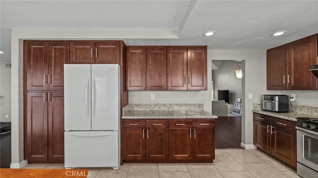 kitchen featuring stainless steel gas range oven, light stone counters, white refrigerator, a textured ceiling, and light tile patterned floors