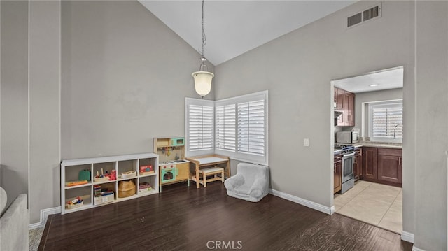 game room featuring light wood-type flooring, high vaulted ceiling, and sink