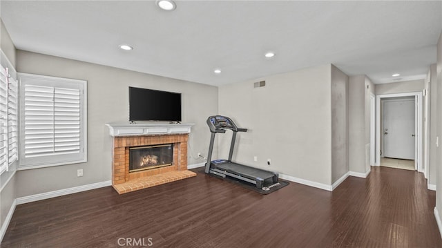 workout area with dark hardwood / wood-style flooring and a brick fireplace