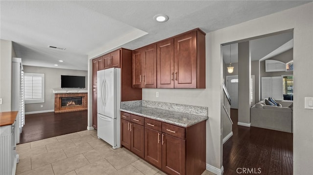 kitchen featuring light hardwood / wood-style floors, light stone countertops, a textured ceiling, a fireplace, and white fridge