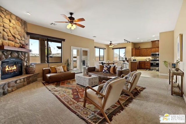 living room with a stone fireplace, ceiling fan, and light colored carpet