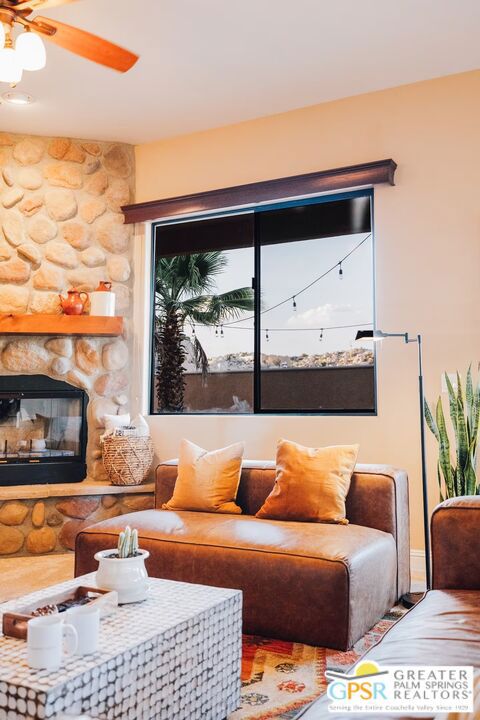 living room featuring a stone fireplace and ceiling fan