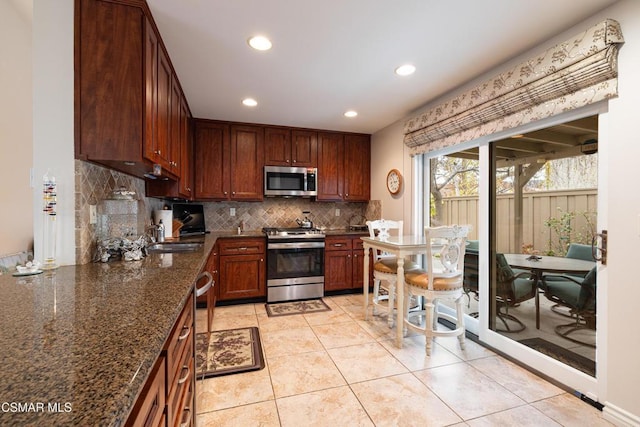 kitchen with appliances with stainless steel finishes, tasteful backsplash, dark stone countertops, sink, and light tile patterned floors