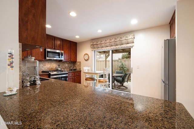 kitchen featuring tasteful backsplash, kitchen peninsula, dark stone counters, and stainless steel appliances