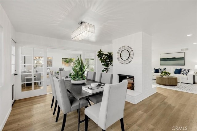 dining space with a multi sided fireplace, light wood-type flooring, and a chandelier