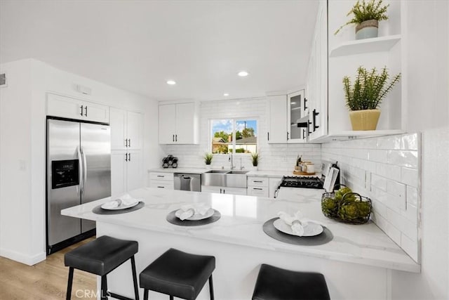 kitchen with sink, light hardwood / wood-style flooring, kitchen peninsula, white cabinets, and appliances with stainless steel finishes