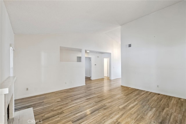 unfurnished living room featuring a textured ceiling, light hardwood / wood-style flooring, and vaulted ceiling