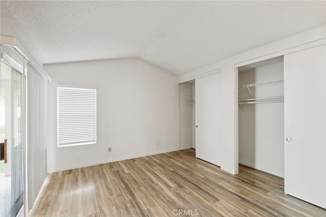 unfurnished bedroom featuring wood-type flooring, two closets, multiple windows, and lofted ceiling