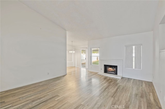 unfurnished living room featuring a chandelier, vaulted ceiling, light hardwood / wood-style floors, and a brick fireplace