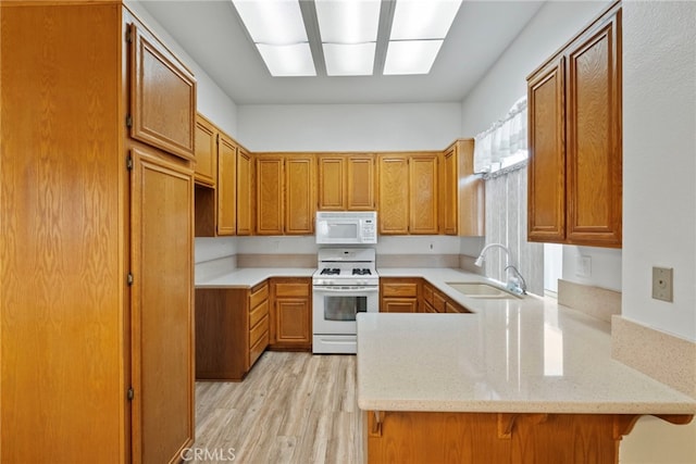 kitchen with sink, a kitchen breakfast bar, kitchen peninsula, white appliances, and light wood-type flooring