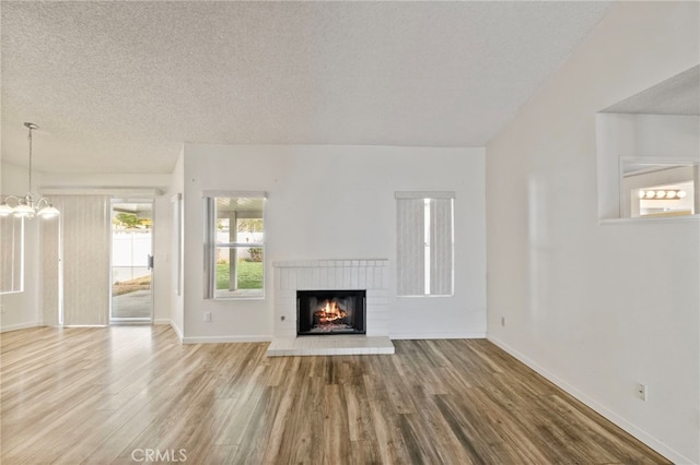 unfurnished living room with a fireplace, a textured ceiling, hardwood / wood-style flooring, and a chandelier