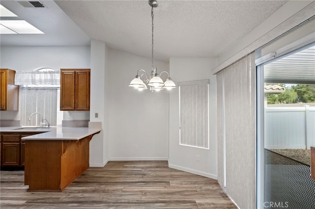 kitchen featuring sink, hanging light fixtures, an inviting chandelier, light hardwood / wood-style flooring, and kitchen peninsula