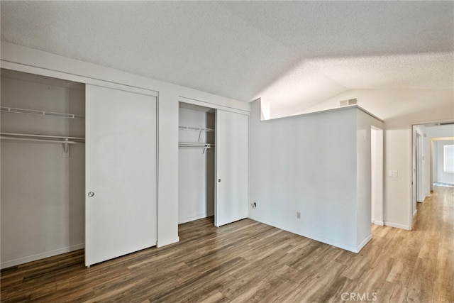 unfurnished bedroom featuring a textured ceiling, hardwood / wood-style flooring, multiple closets, and lofted ceiling