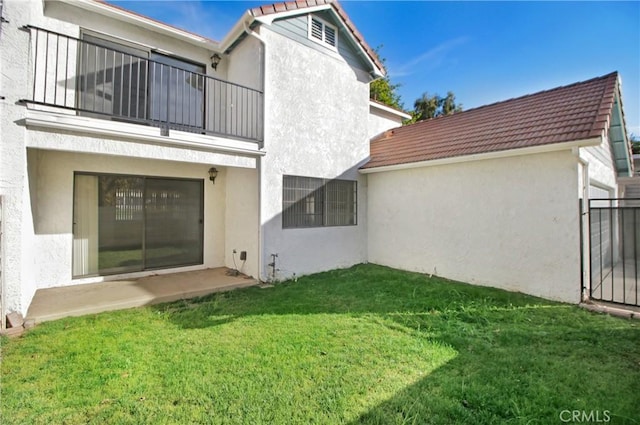 rear view of property with a balcony, a patio area, and a lawn