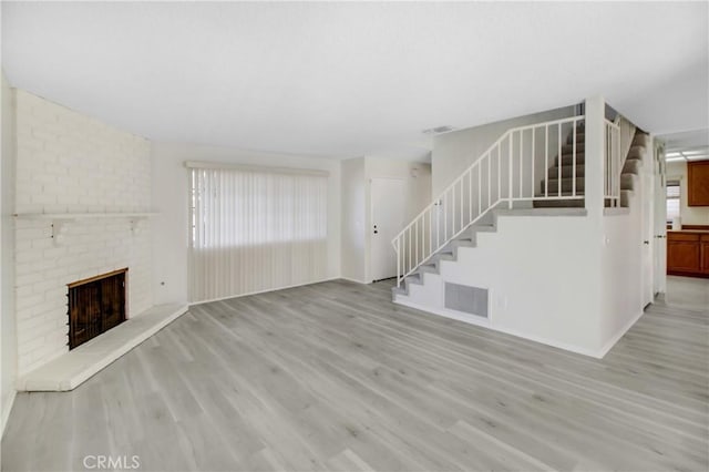 unfurnished living room with a brick fireplace and light wood-type flooring