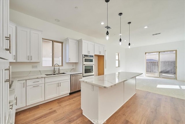 kitchen with a center island, sink, hanging light fixtures, white cabinetry, and stainless steel appliances