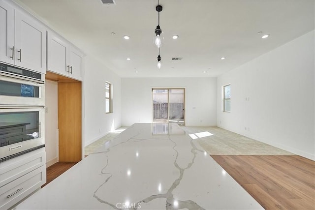 kitchen featuring light stone countertops, double oven, decorative light fixtures, light hardwood / wood-style floors, and white cabinetry