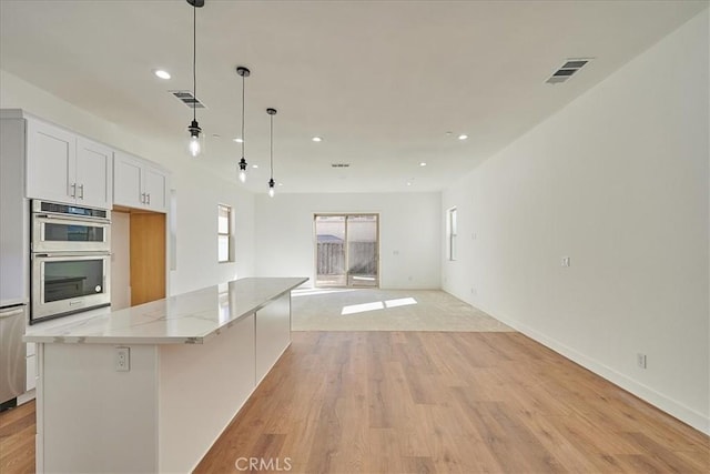 kitchen featuring light stone counters, stainless steel double oven, pendant lighting, white cabinets, and a large island