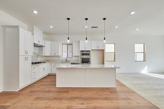 kitchen featuring white cabinets, decorative light fixtures, a kitchen island, and sink