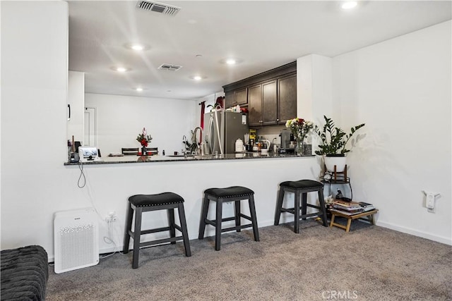 kitchen with a breakfast bar, dark brown cabinetry, stainless steel fridge, and kitchen peninsula