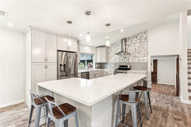 kitchen featuring appliances with stainless steel finishes, pendant lighting, wall chimney exhaust hood, light stone countertops, and light hardwood / wood-style flooring