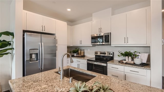 kitchen featuring decorative backsplash, light stone counters, stainless steel appliances, sink, and white cabinetry