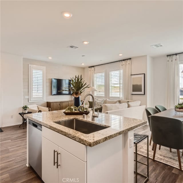 kitchen featuring dark wood-type flooring, a center island with sink, sink, stainless steel dishwasher, and white cabinetry