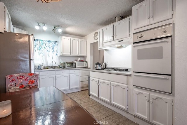 1119 E Colon St, Wilmington, CA 90744 - kitchen featuring a warming drawer, stainless steel appliances, white cabinets, under cabinet range hood, and a textured ceiling