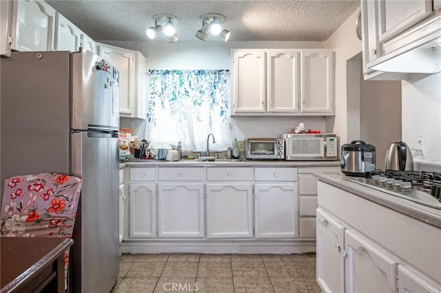 kitchen featuring sink, white cabinets, a textured ceiling, light tile patterned floors, and appliances with stainless steel finishes