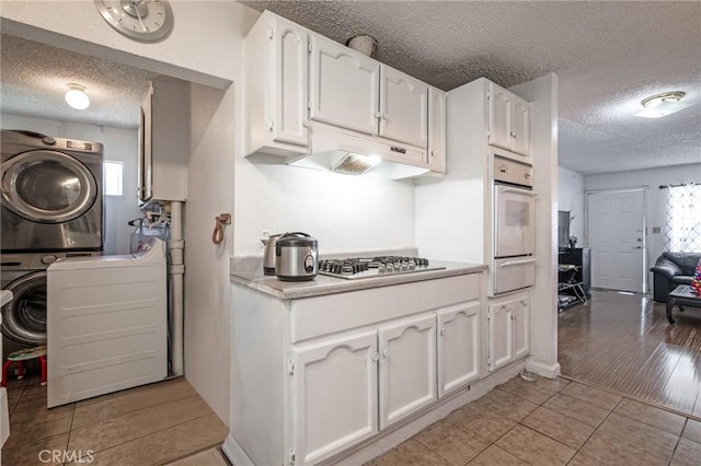 kitchen with white cabinetry, stacked washer and clothes dryer, light hardwood / wood-style floors, oven, and stainless steel gas stovetop