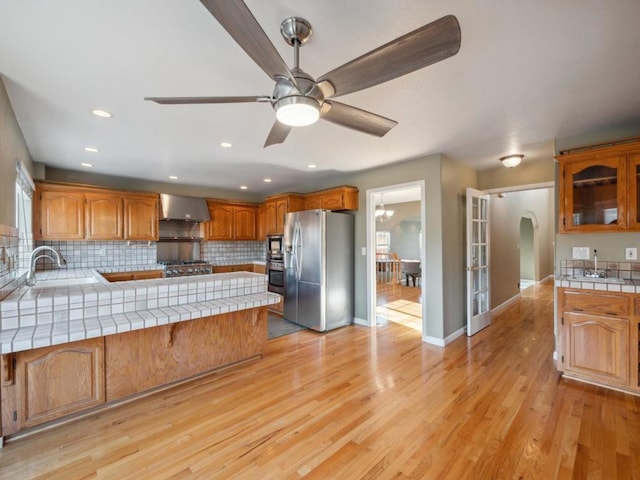 kitchen featuring sink, wall chimney exhaust hood, tile counters, and appliances with stainless steel finishes