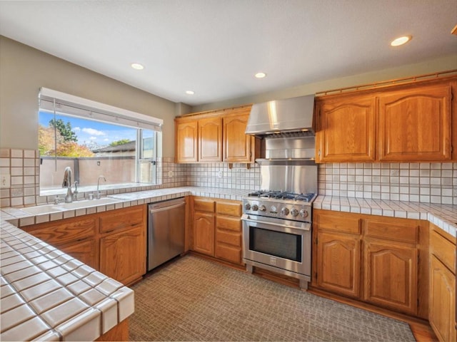 kitchen with tasteful backsplash, wall chimney range hood, sink, stainless steel appliances, and tile countertops