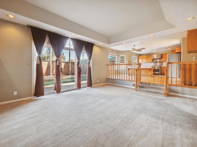 unfurnished living room with ceiling fan, a wealth of natural light, light carpet, and a tray ceiling