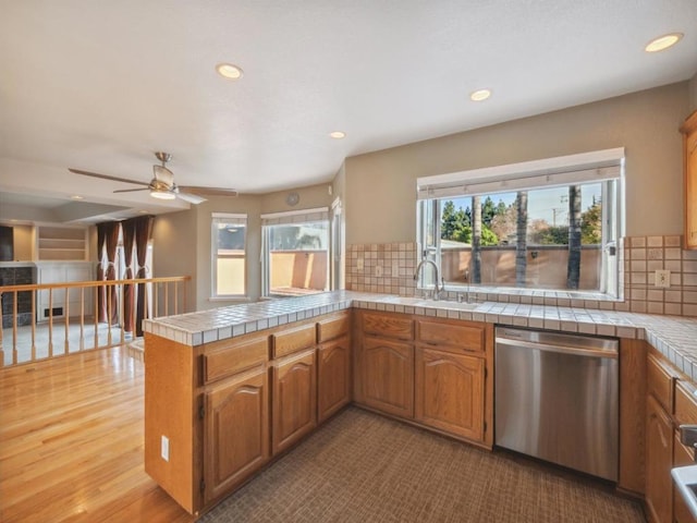 kitchen with kitchen peninsula, stainless steel dishwasher, sink, decorative backsplash, and tile counters