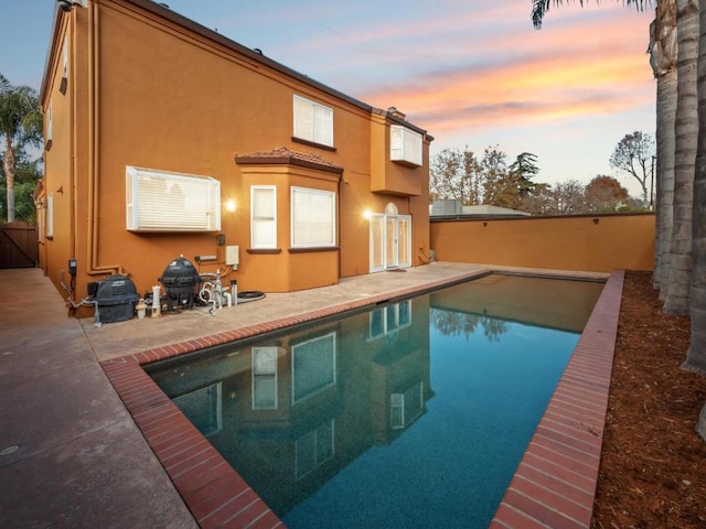 back house at dusk featuring a fenced in pool and a patio area