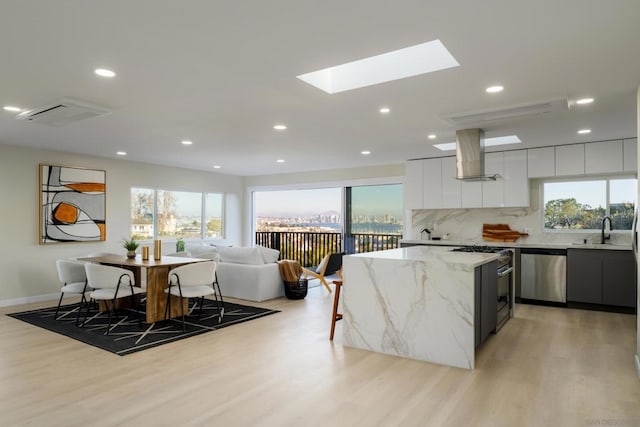 kitchen with a skylight, light stone countertops, stainless steel appliances, range hood, and white cabinets