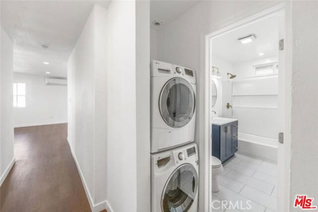 washroom featuring a wall mounted AC, stacked washer and dryer, and dark wood-type flooring