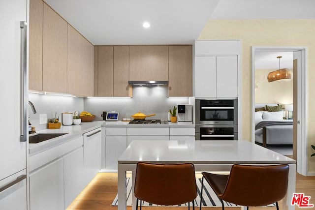 kitchen with stainless steel appliances, light brown cabinetry, decorative backsplash, light wood-type flooring, and sink