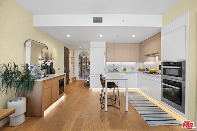 kitchen with a breakfast bar, stainless steel oven, light hardwood / wood-style flooring, and white cabinetry