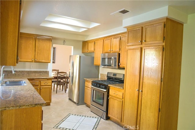 kitchen with light tile patterned floors, a skylight, stainless steel appliances, dark stone countertops, and sink